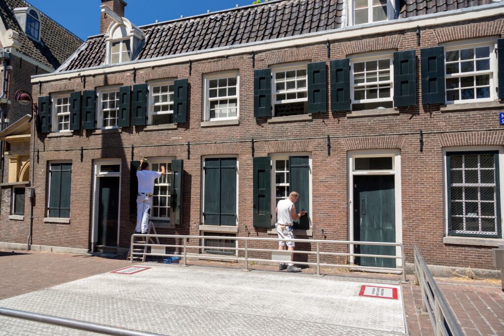 Two painters refurbishing the traditional Dutch brick house facade on a sunny day.